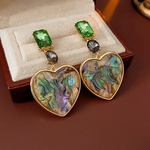 Detailed shot of green crystal and heart abalone shell earrings in a jewelry box