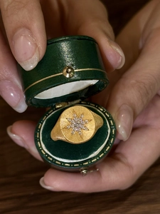 Macro shot of gold starburst signet ring with inlaid gems in a vintage green gift box