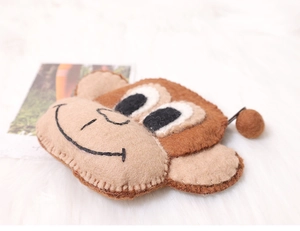 Detailed close-up of a monkey-shaped wool felt wallet with embroidery on soft background