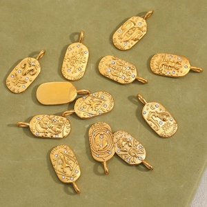 Flat lay of 12 gold-plated stainless steel zodiac sign pendants on green fabric
