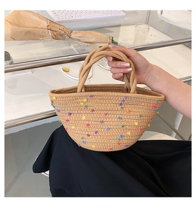 Detail of handmade straw bucket bag with colorful pompom accents and woven handles