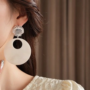 Detail of large silver starfish and shell round earrings worn by model for beach style