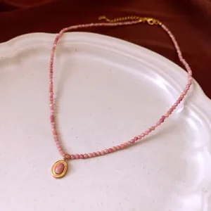 Pink stone beaded necklace with vintage gold oval pendant on a ceramic tray