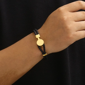 Detail of a black braided leather double-layer bracelet with a gold circular metal plate