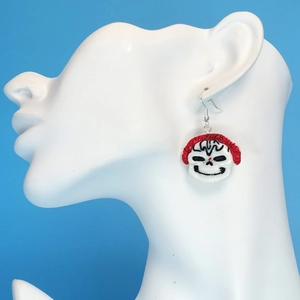 Detail view of a punk skull earring with red mohawk on a white display stand