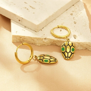 Detail of golden snake hoop earrings with green enamel eyes on stone background