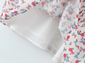 Close-up of white dress hem featuring delicate red and blue floral embroidery and lining