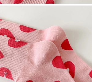 Macro detail of pink knit sock heel featuring red heart patterns and ribbed texture