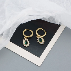 Detailed macro of gold emerald zircon hoop earrings on white translucent fabric