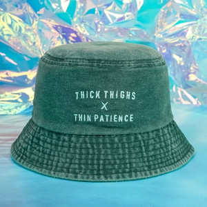 Close-up of white embroidery on dark green washed denim bucket hat with quilted brim