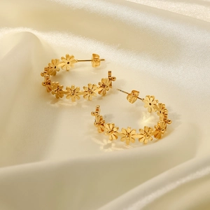 Pendientes de aro en C con forma de flor dorada sobre elegante seda beige y luz suave