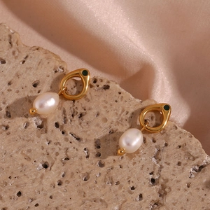 Close-up of gold pearl earrings with green gemstones on a textured stone surface