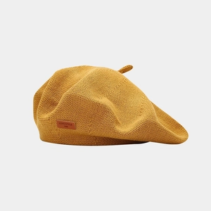 Dettaglio del basco giallo in maglia con etichetta in pelle marrone e testo inciso