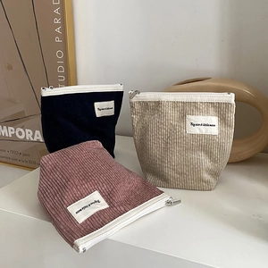 Three corduroy cosmetic bags in black, beige, and pink colors on a white surface