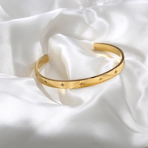 Detail shot of gold-plated bangle with engraved star patterns and zircon inlays on white silk