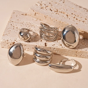 Minimalist silver geometric rings with organic and multi-layer designs on beige travertine