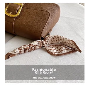 Detail of brown litchi textured leather handbag with gold buckle and silk scarf handle