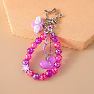 Macro view of purple beaded keychain with heart and wing charms on a beige background