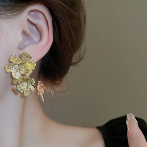 Close-up of double floral earrings with textured gold metallic petals on ear