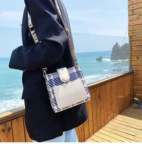 Detail of plaid tweed crossbody bucket bag showing wide strap and buckle on model