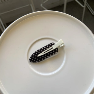 Detail of polka dot duckbill hair clip in iron shape on a white round display tray