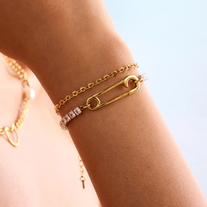 Elegant gold chain bracelet set with cubic zirconia safety pin charms on a model's wrist
