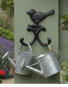 Detail von Vintage-Vogelhaken aus Gusseisen mit Gießkannen vor einem Gartenhintergrund