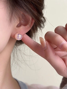 Close-up of iridescent pink mermaid pearl studs worn on ear showing shimmering luster