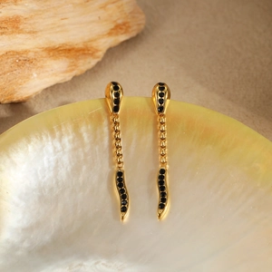 Gold snake earrings for women with black zircon stones displayed on a pearl shell