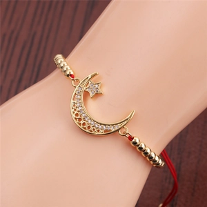 Detailed close-up of golden crescent moon and star charm bracelet with red braided cord