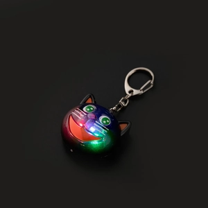 Detail of colorful glowing cat-head keychain with LED light and metal hook on black background