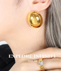 Detail of mirror-finish gold oval stud earrings and textured zircon ring on a model