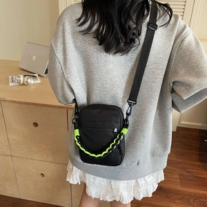 Close-up of black nylon shoulder bag with a neon green woven chain in a home setting