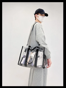Detailed shot of transparent PVC tote bag with black trim worn by a model in a studio
