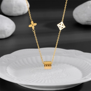 Detail of gold metal necklace featuring a cylindrical pendant with floral charms on a tray