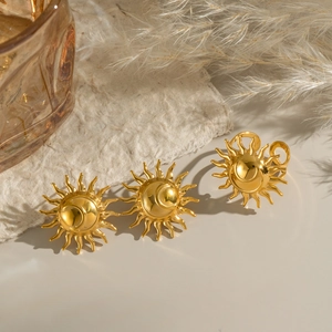 Detail of golden sun-shaped earring and ring set on minimalist warm fabric backdrop