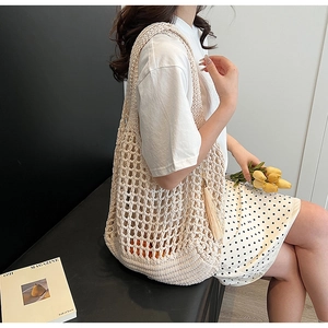 Detail of a beige woven knit tote bag with tassel trim held by a model in a summer setting