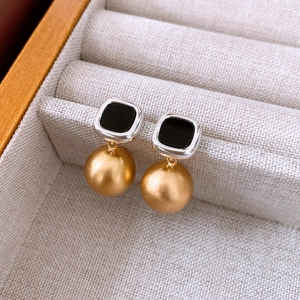 Detail of square acetate stud earrings with matte gold spheres on linen texture