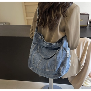 Détail des bords effilochés d'un grand sac cabas en denim bleu délavé porté par un modèle
