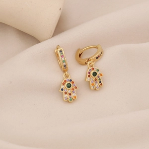 Macro shot of gold Hamsa hand earrings with colorful cubic zirconia on fabric