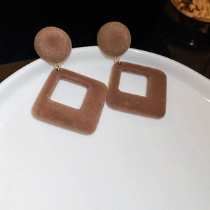 Détail de boucles d'oreilles géométriques floquées marron foncé sur un plateau en céramique