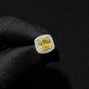 Macro detail of cushion cut yellow zircon halo earrings held in gloved hand on black background