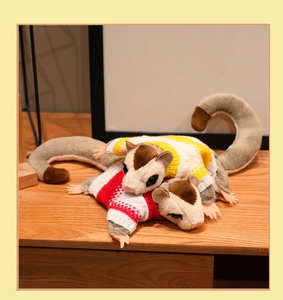 Close-up of sugar glider plushies wearing yellow and red knitted sweaters on a wooden surface