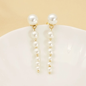 Detail of long drop pearl earrings with six graduated white pearls on gold-plated metal