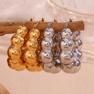 Polished gold and silver cloud bead hoop earrings on a minimalist wooden display stand