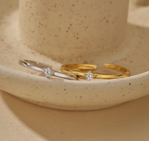 Detail view of gold and silver minimalist open rings with micro-set diamonds on ceramic