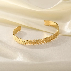 Macro detail of golden feather leaf textures on a stainless steel open cuff bracelet