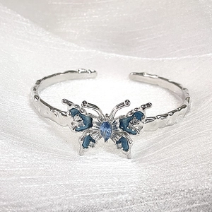 Bracciale aperto farfalla smalto blu con pietra marquise e cristalli scintillanti su stoffa bianca