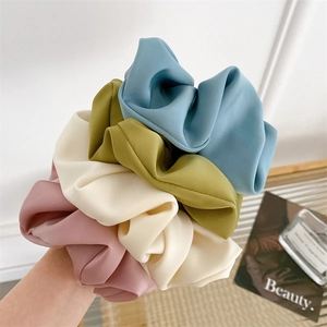 Close-up of four Morandi colored satin scrunchies in blue, green, beige and pink tones