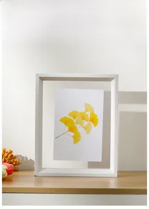Close-up of minimalist white photo frame with ginkgo leaf art on a wooden surface